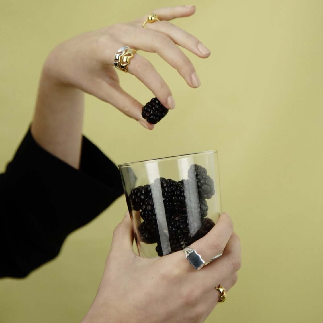 Close up of a women with rings, dropping a blackberry in a glass filled with blackberries