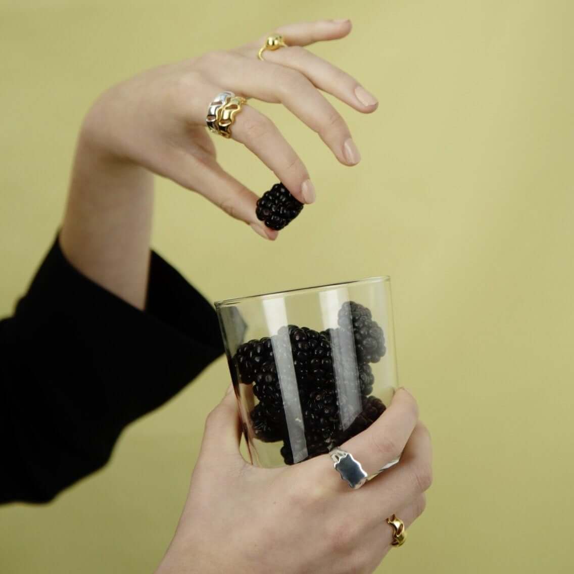 Close up of female hands with rings, dropping a blackberry in a glass filled with blackberries