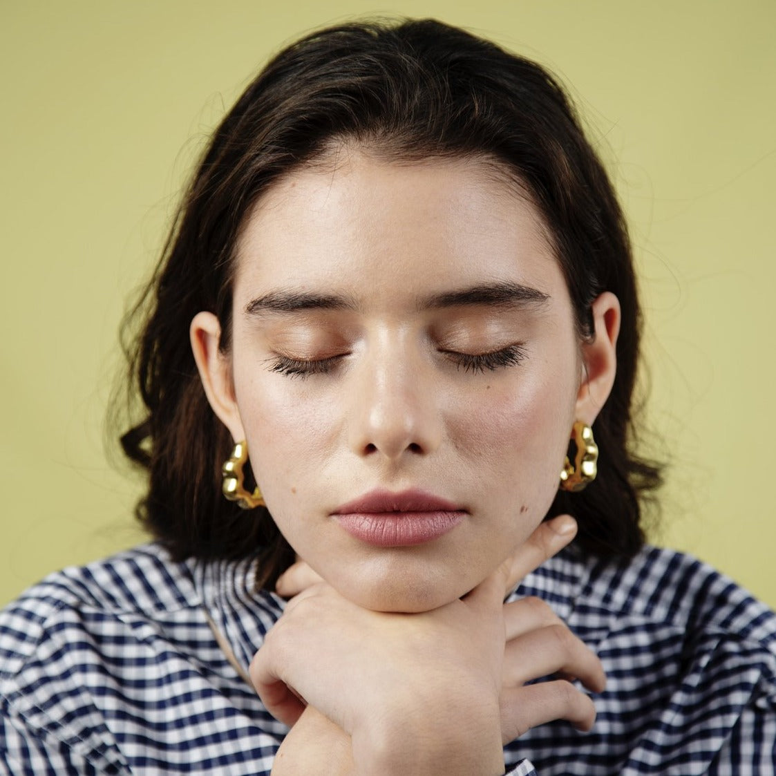 Close up of woman with closed eyes leaning on her folded hands. Wearing gold earrings