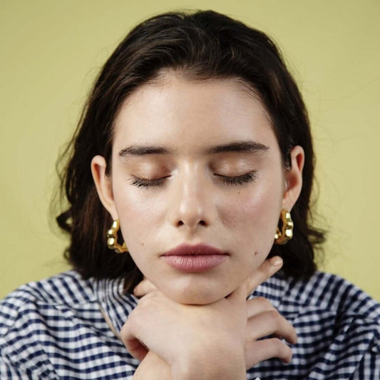 Close up of woman with closed eyes leaning on her folded hands. Wearing gold earrings.