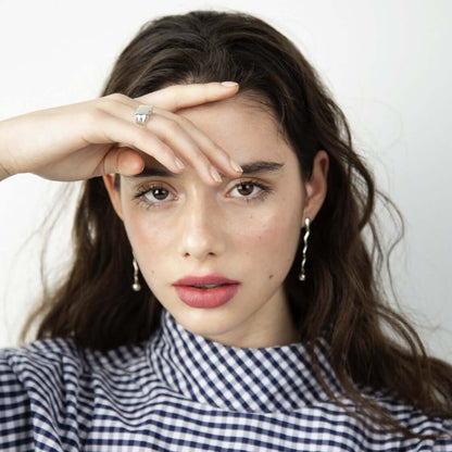 Woman looking into camera, holding her hand over her forehead and eye. Wearing earrings
