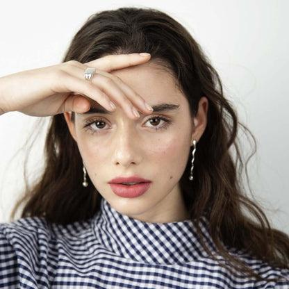 Woman looking into camera, holding her hand over her forehead and eye. Wearing earrings