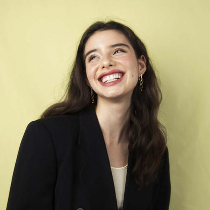 Woman with a big smile, looking to the side. Wearing black blazer and earrings