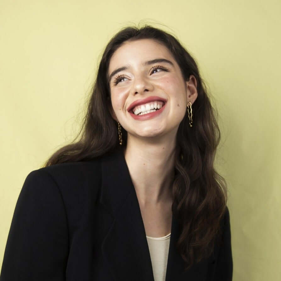 Woman with a big smile, looking to the side. Wearing black blazer and earrings
