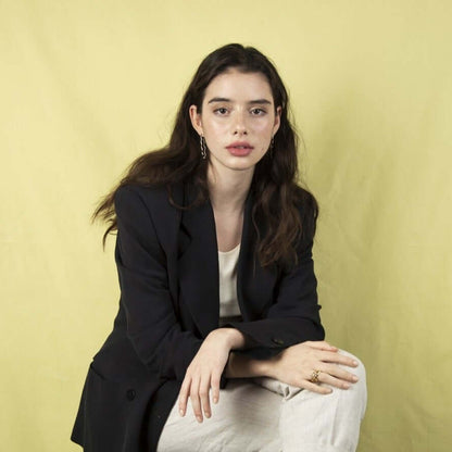 Woman sitting on a chair looking serious into the camera. Wearing a black blazer. Crossed hands and legs.