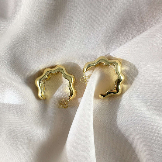 Product photo of a pair of wavy gold hoops laying on a light textile