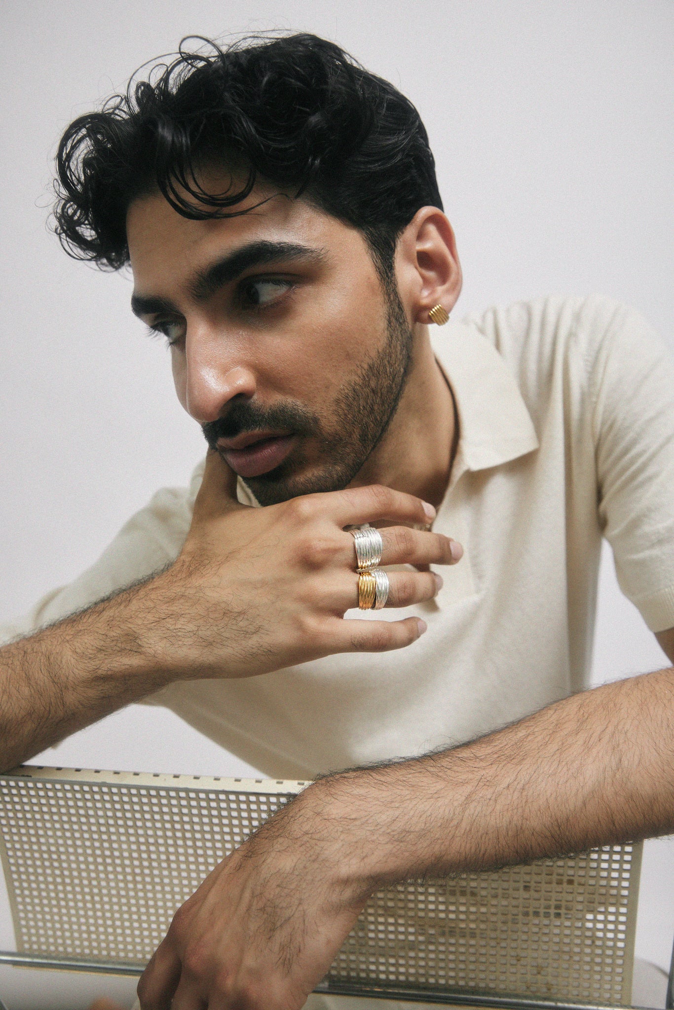 Man poses on chair, wearing many rings