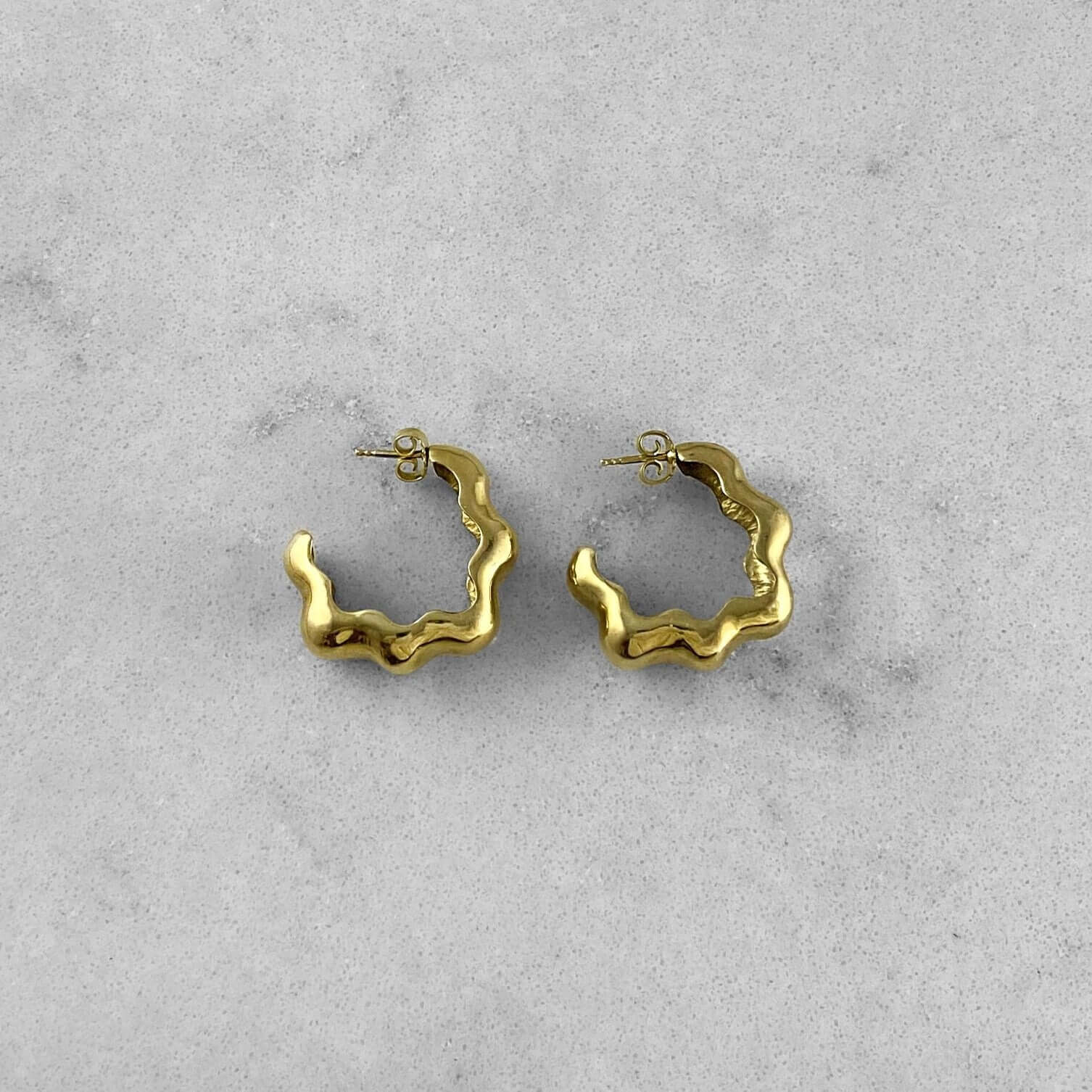 Product photo of a pair of gold hoops laying on marble