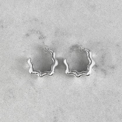 Product photo of a pair of silver hoops laying on marble