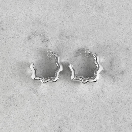 Product photo of a pair of silver hoops laying on marble