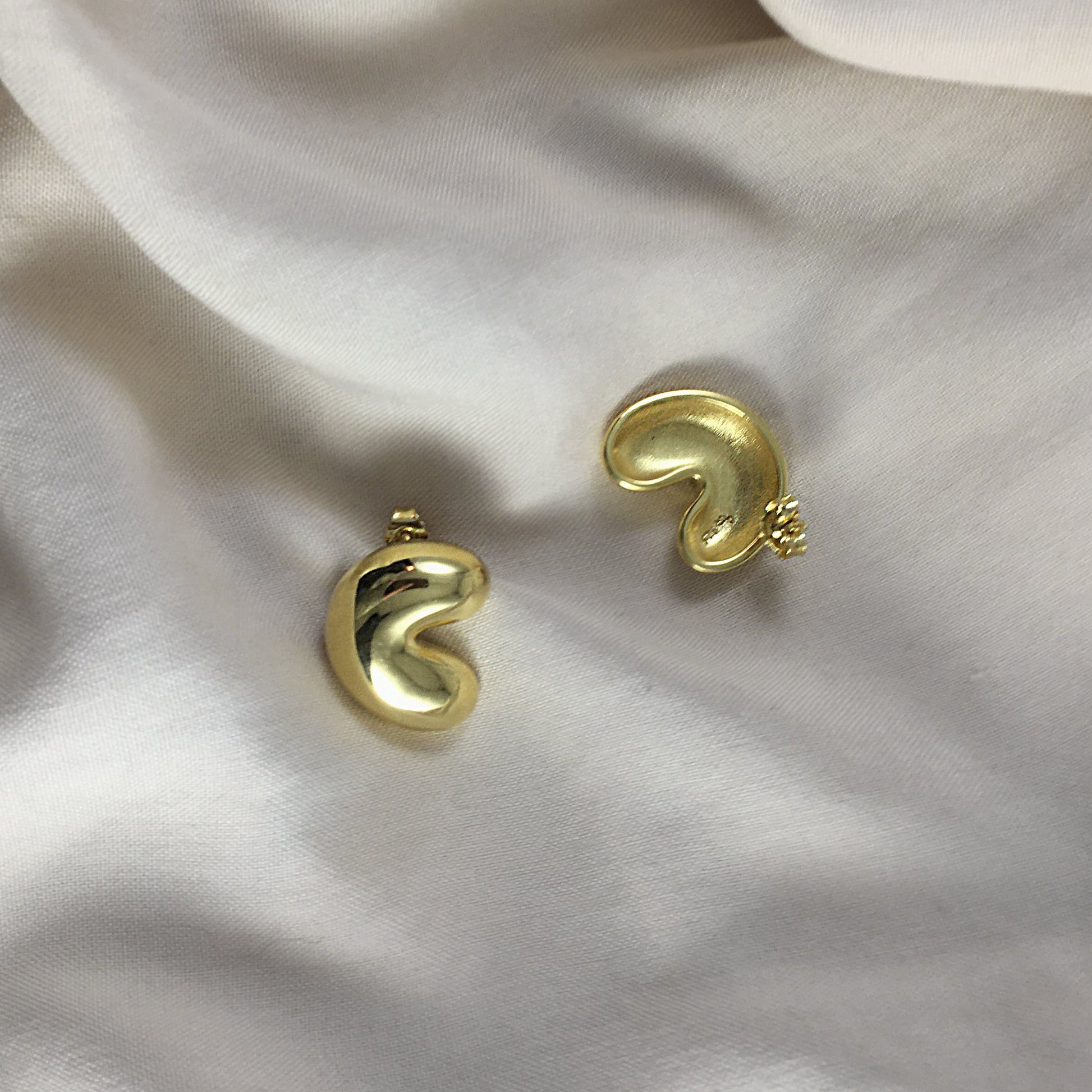 A pair of gold earrings laying on a light textile