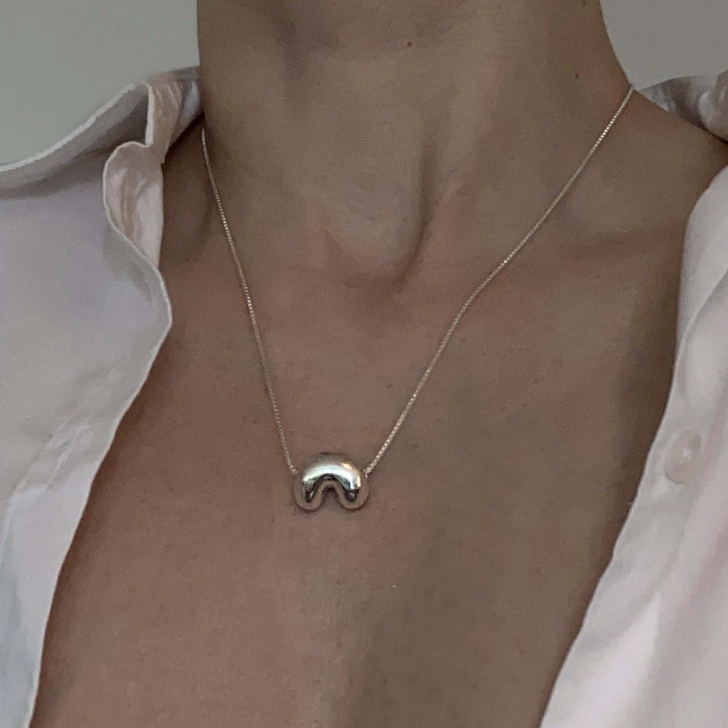 Close up on female neck and chest, wearing silver necklace with pendant