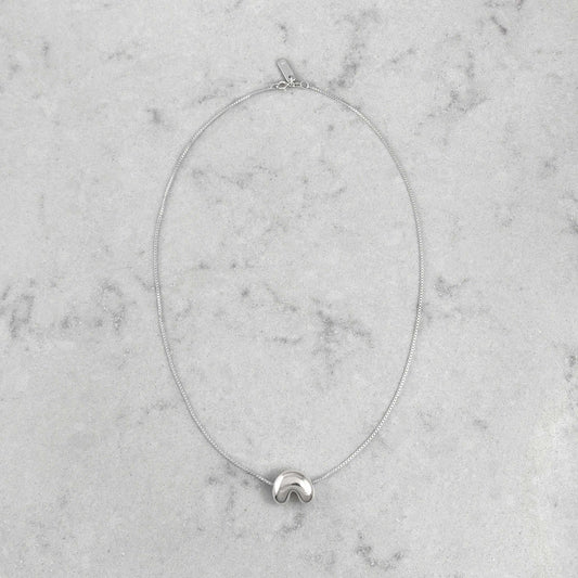 Product photo of a silver necklace by Aur Studio. On a marble plate