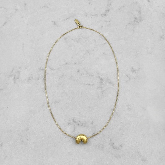 Product photo of a gold necklace by Aur Studio. On a marble plate