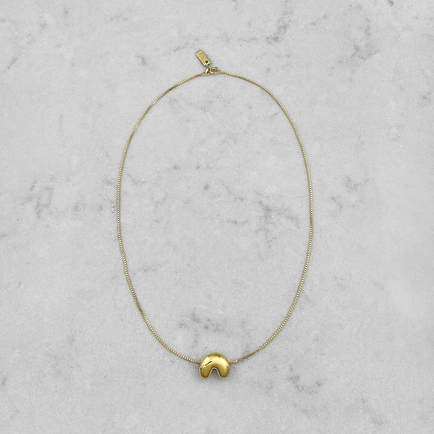 Product photo of a gold necklace by Aur Studio. On a marble plate