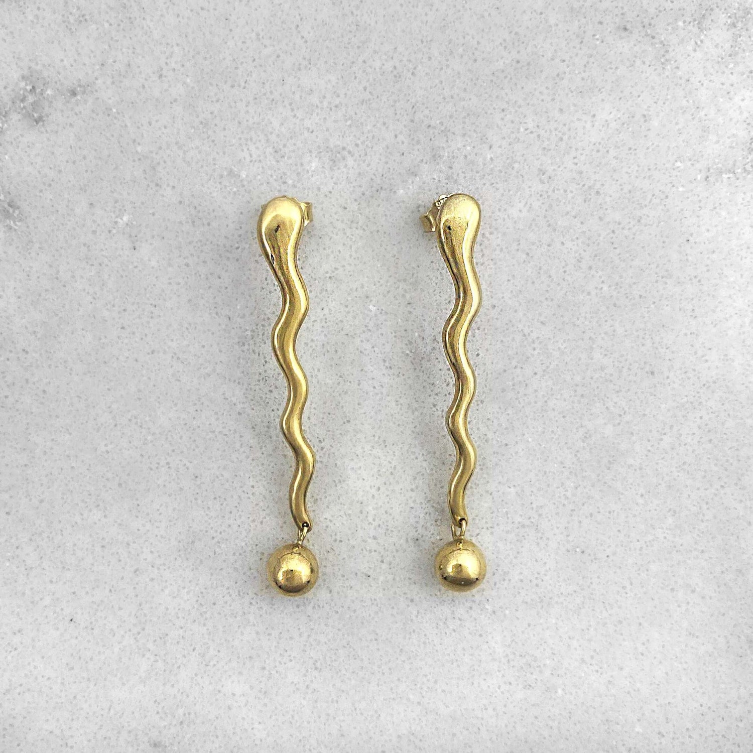 Product photo of a pair of gold earrings on a marble plate