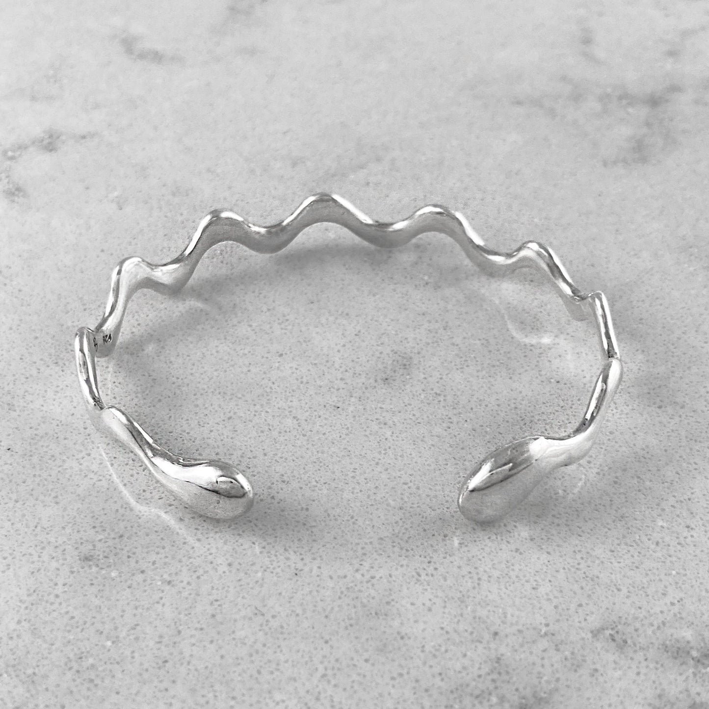 Product photo of a silver bracelet laying on a marble plate