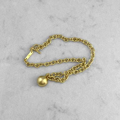 Product photo of a gold chain necklace with pendant, laying on a marble plate