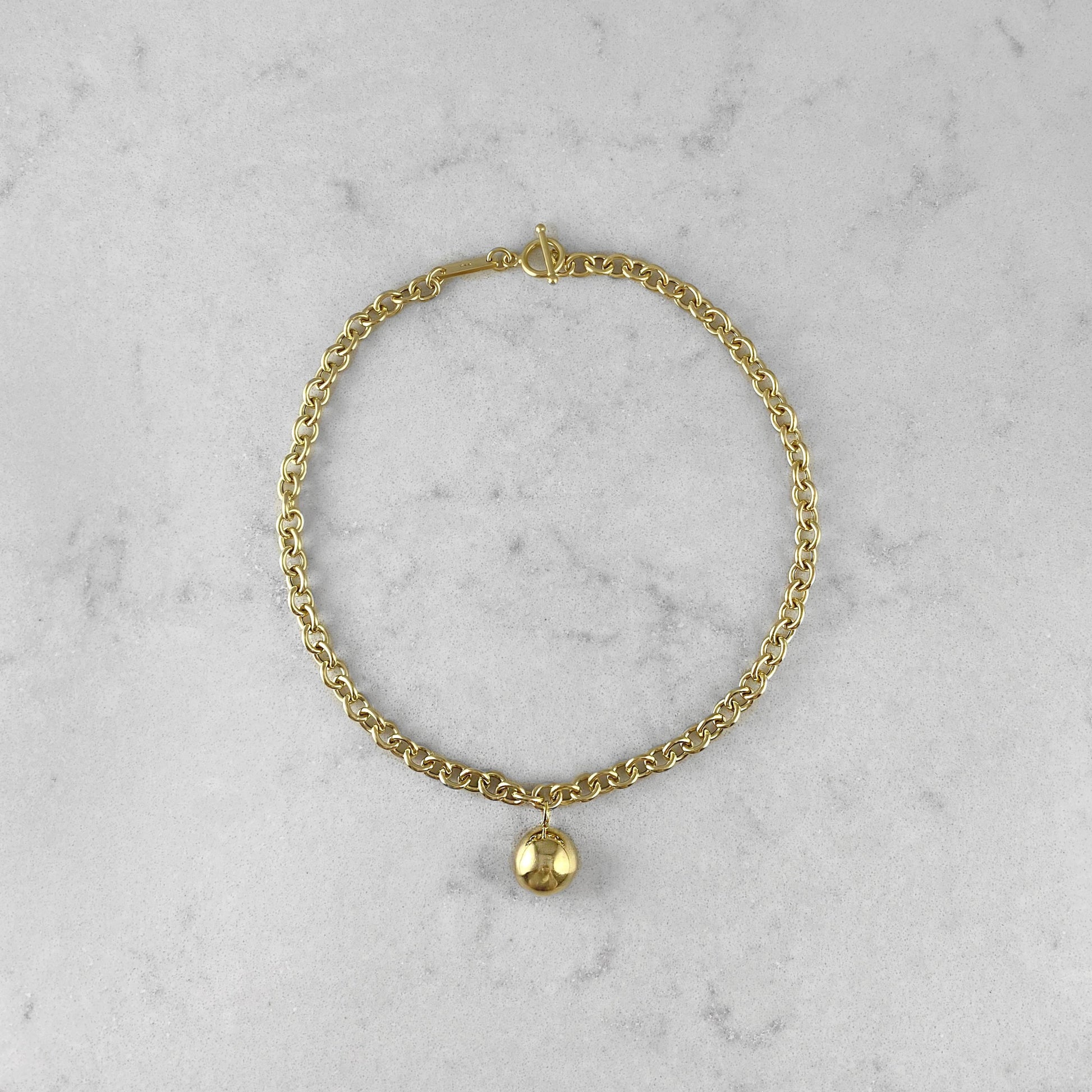 Product photo of a gold chain necklace with pendant, laying on a marble plate