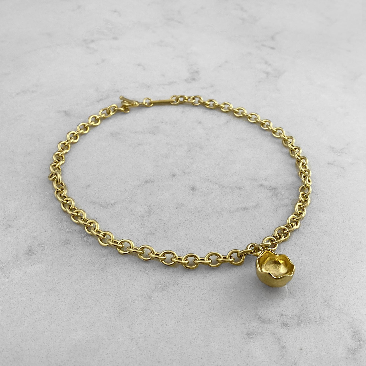 Product photo of a gold chain necklace with pendant, laying on a marble plate
