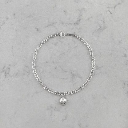 Product photo of a silver chain necklace with pendant, laying on a marble plate