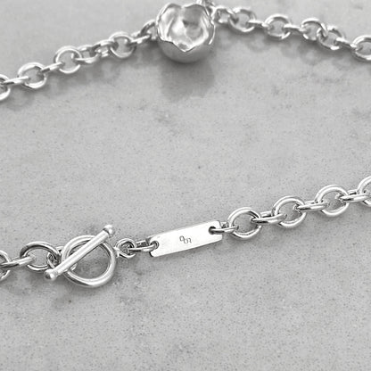 Close up og details of a silver chain necklace with pendant, laying on a marble plate