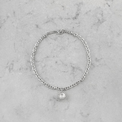 Product photo of a silver chain necklace with pendant, laying on a marble plate