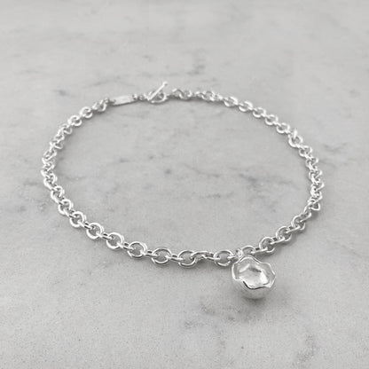 Product photo of a silver chain necklace with pendant, laying on a marble plate